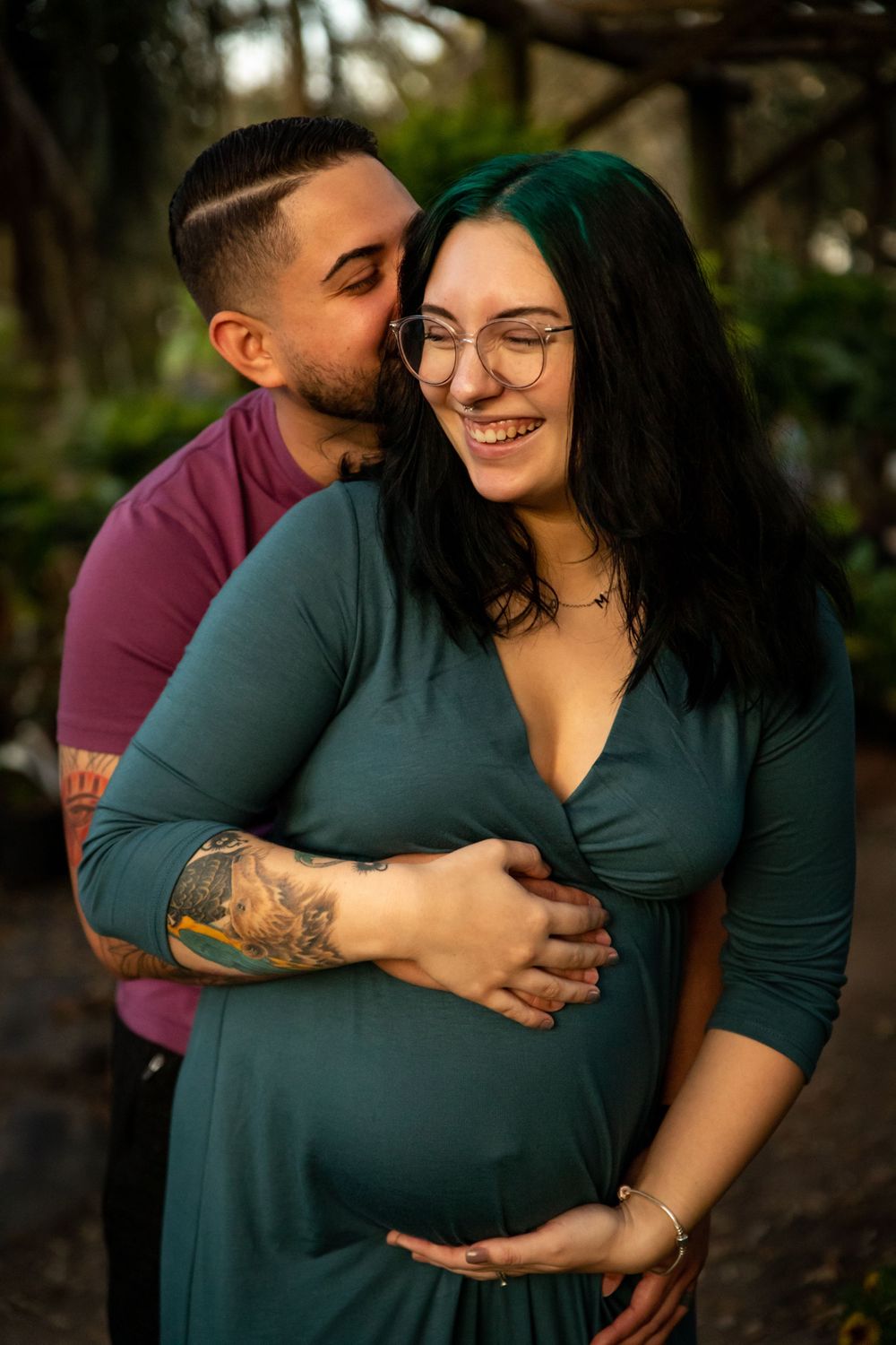 Expecting couple sharing a tender moment outdoors, man kissing pregnant womans cheek while holding her belly.