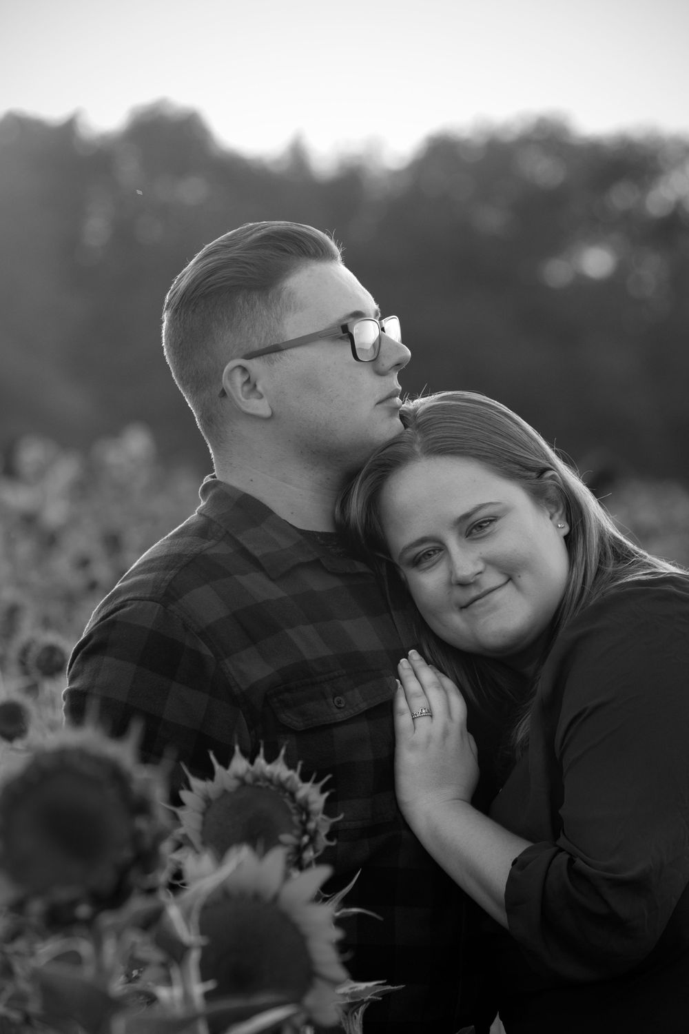 Black and white photo of couple embracing tenderly in sunflower field at golden hour.