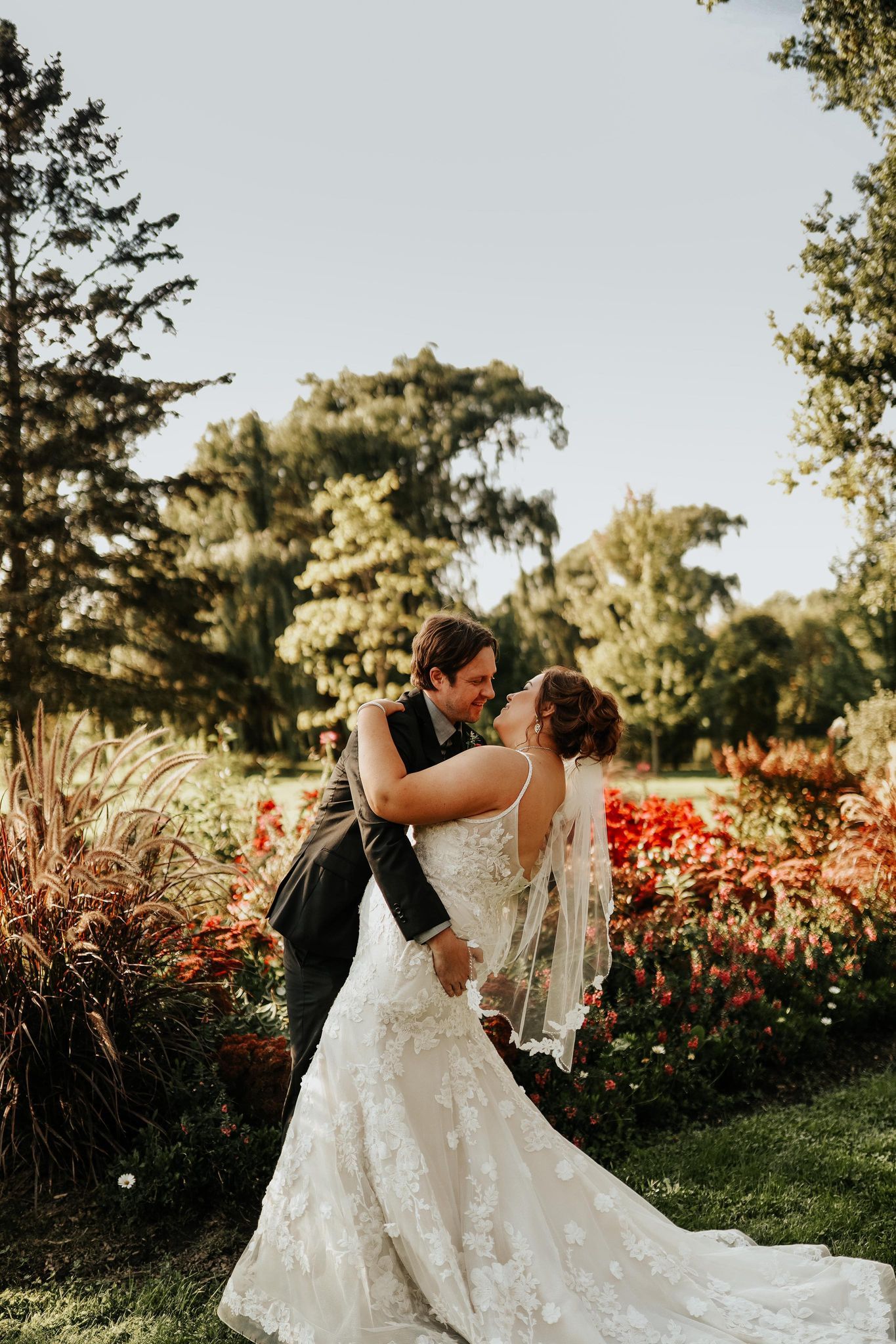 A romantic wedding dip kiss in a garden with red flowers during golden hour.