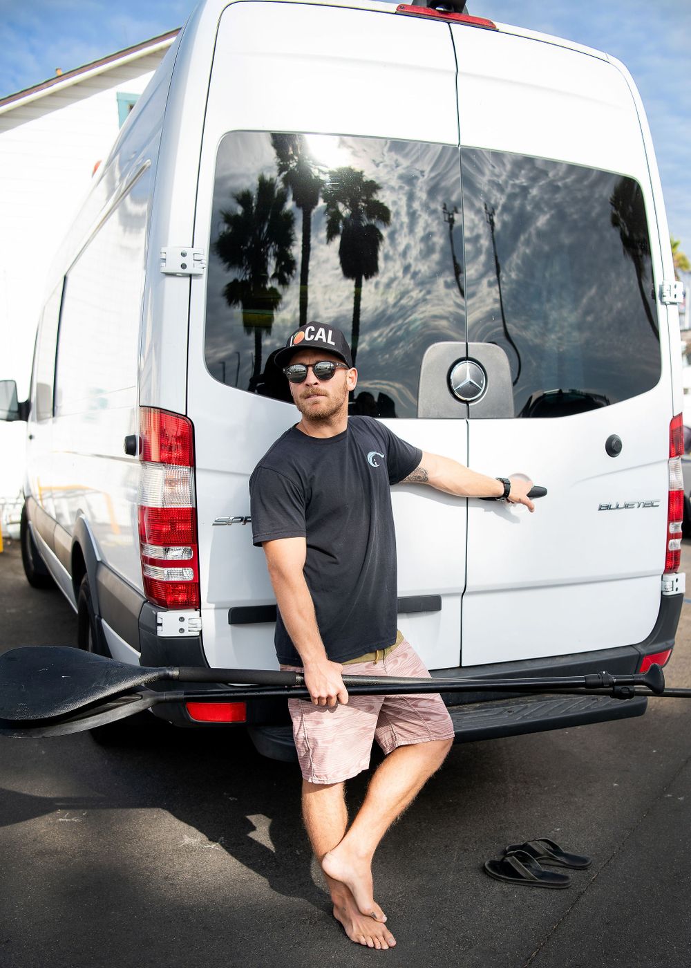 man standing at the back of a white sprinter van with palm trees reflected in the windows santa barbara ca