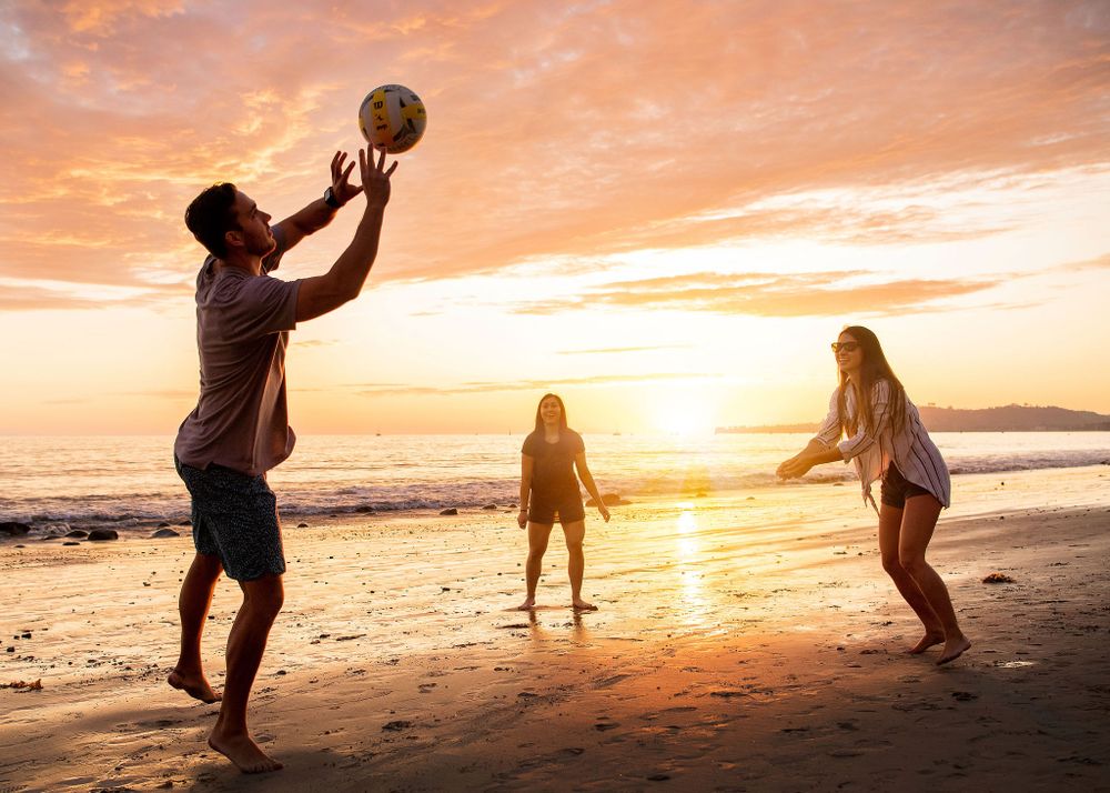 silhouette of friends playing volleyball at the beach in santa barbara ca with a golden orange sunset behind them
