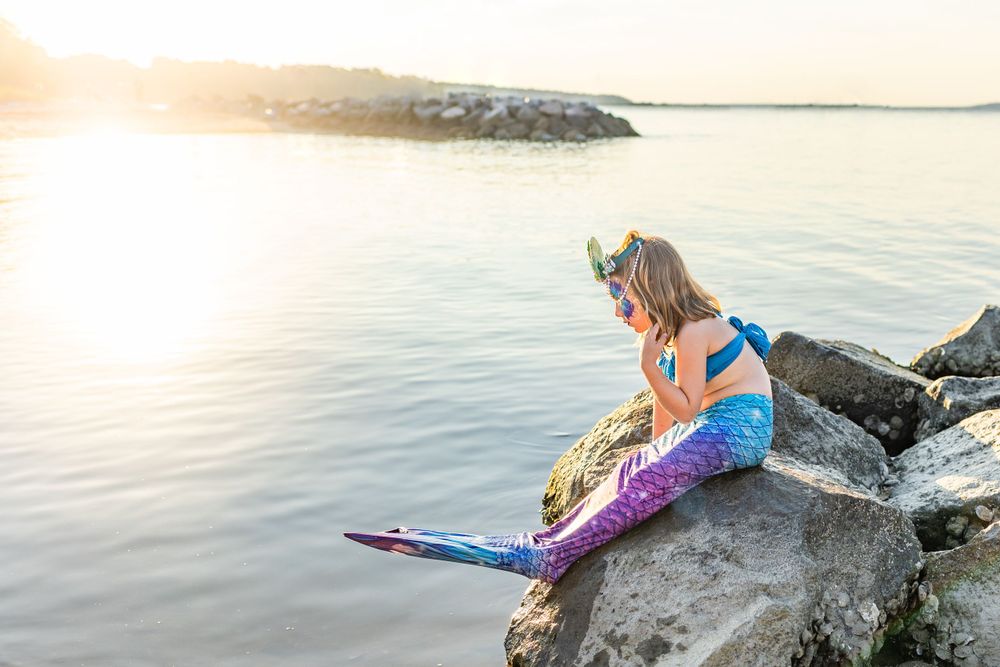 Mermaid costume silhouette against sunset on rocky beach overlook.