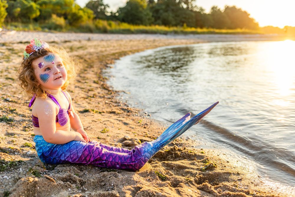 Mermaid tail sparkles in golden sunset light on sandy beach.