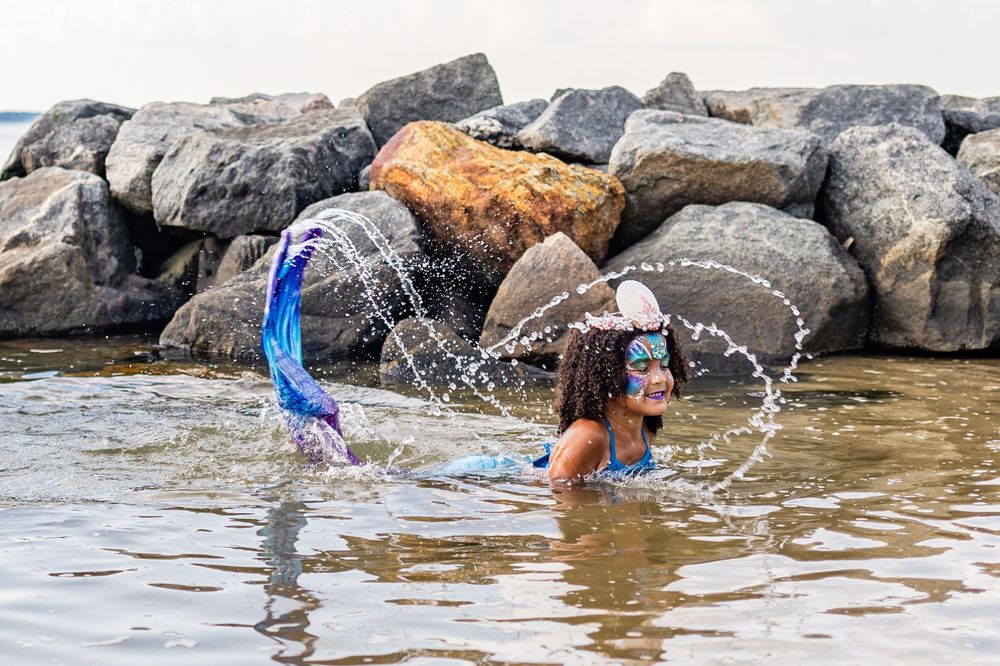 Splashing water creates arcs while playing in shallow rocky water near shore.
