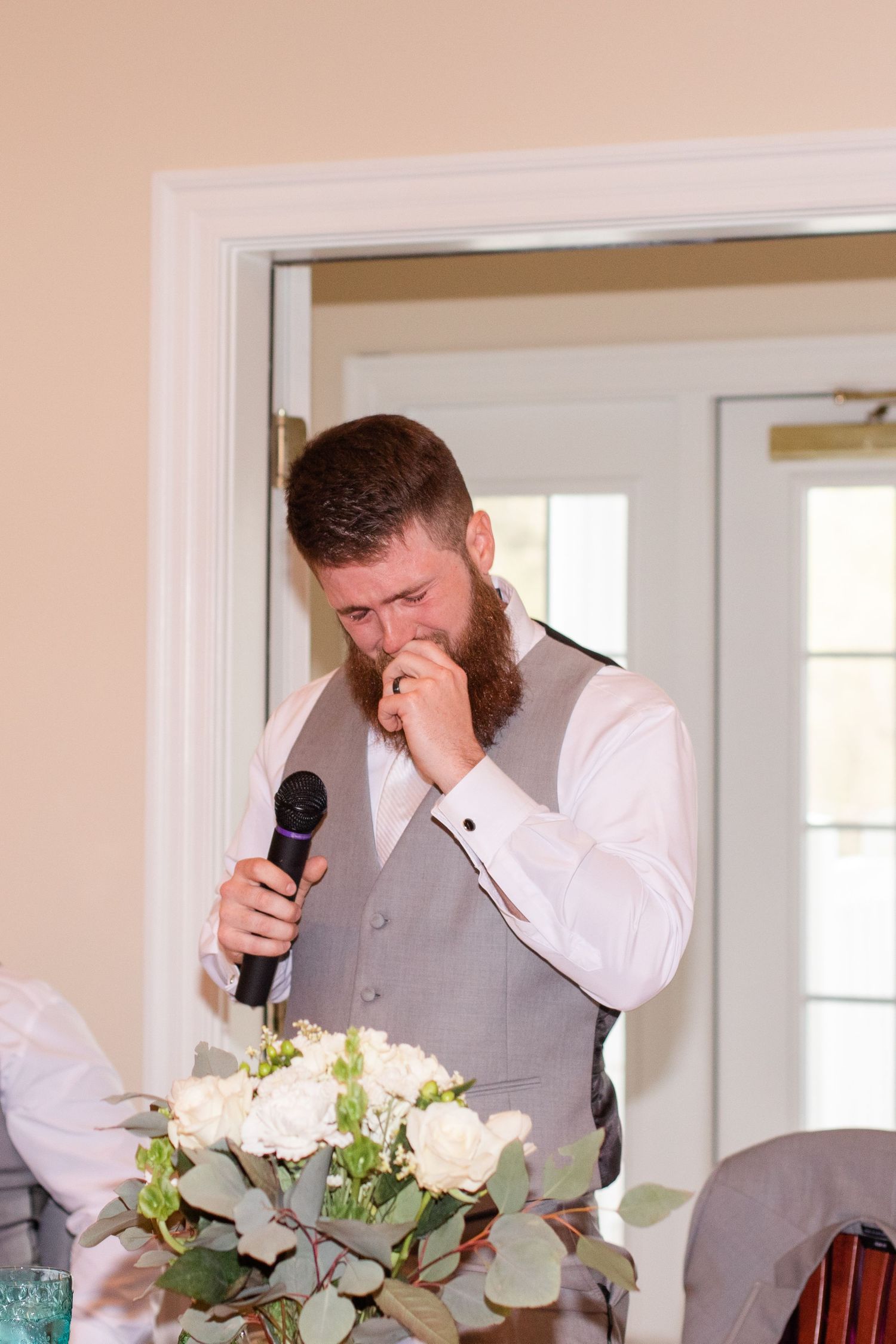 Emotional moment during wedding speeches with floral centerpieces in foreground.