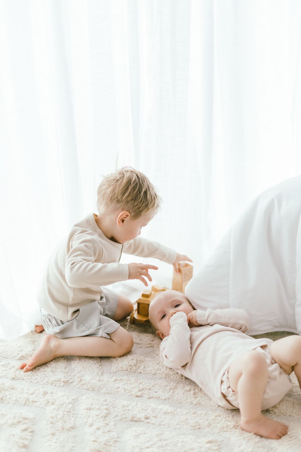 Two young children play together on plush white carpet.
