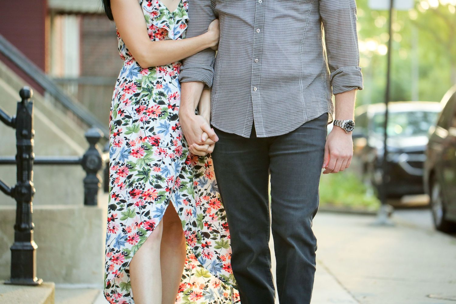 A couple holding hands while walking on a city sidewalk with a floral dress and casual attire.