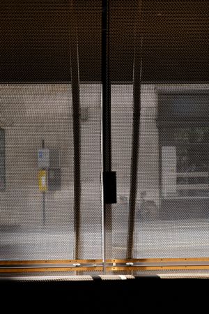 View through vertical dark poles and mesh screen showing a blurry urban street scene with yellow signage in the background.