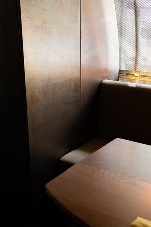 Modern interior space with wooden table corner and dark wall illuminated by natural window light.