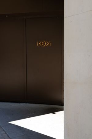 Gold Kona sign mounted on dark brown wall with dramatic shadow and light contrast in minimalist architectural setting.