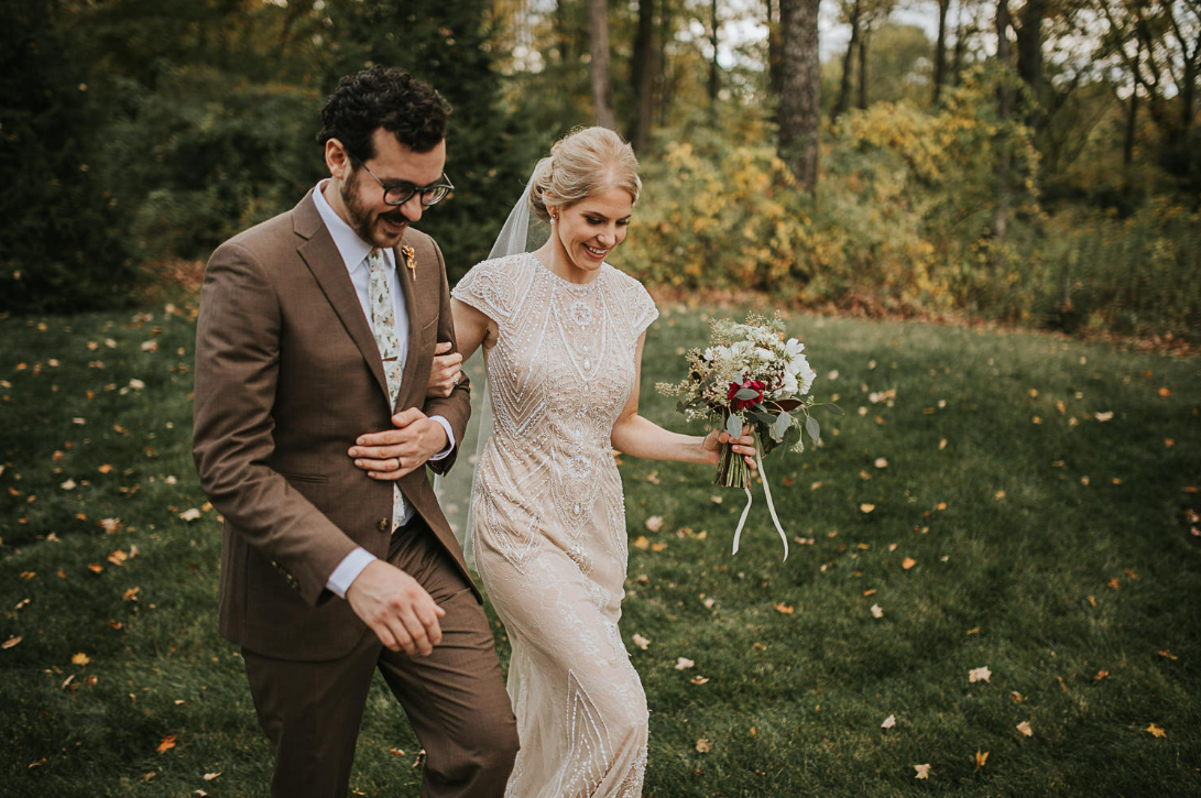 A couple walking together on grass holding drinks during their fall wedding.