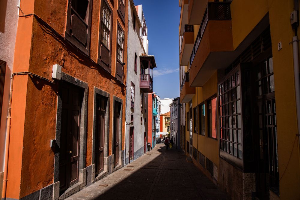 Narrow colorful street with orange and yellow buildings under a bright blue sky in a Spanish town.
