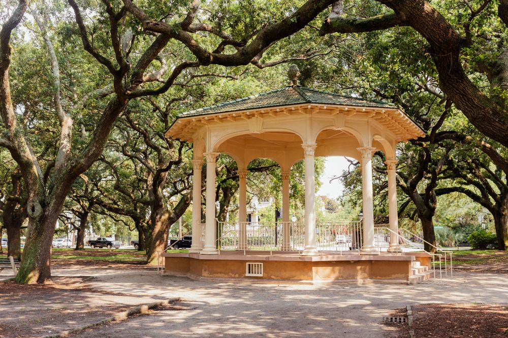 Elegant white gazebo surrounded by sprawling oak trees in a peaceful historic Southern park.