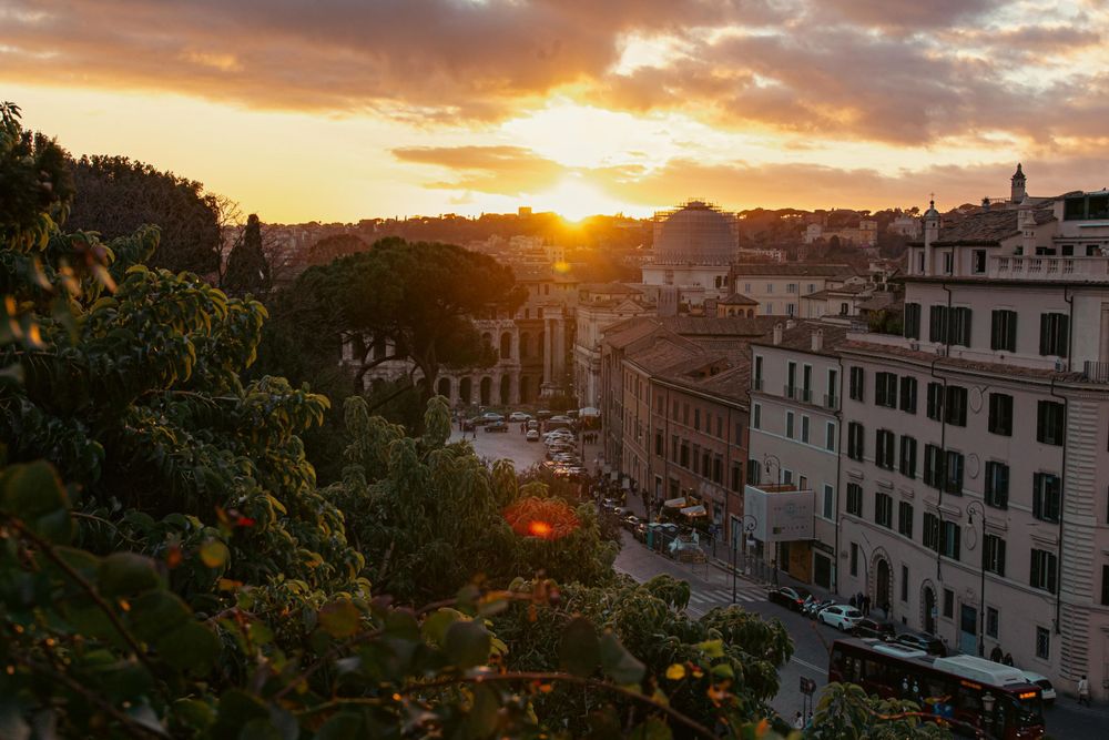 Golden sunset over Rome's ancient cityscape with lush trees and historic buildings glowing in warm evening light.