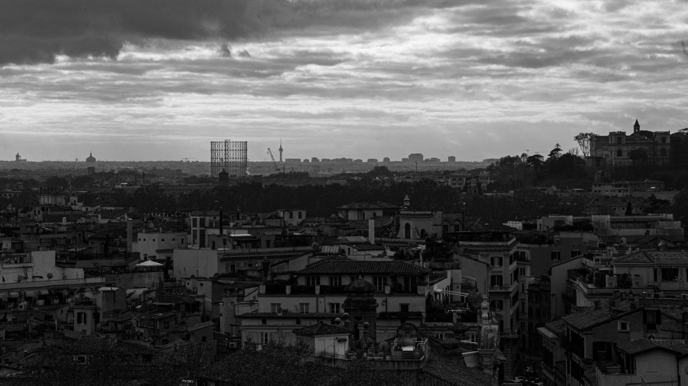 Black and white panoramic view of Rome's sprawling rooftops under dramatic cloudy sky.