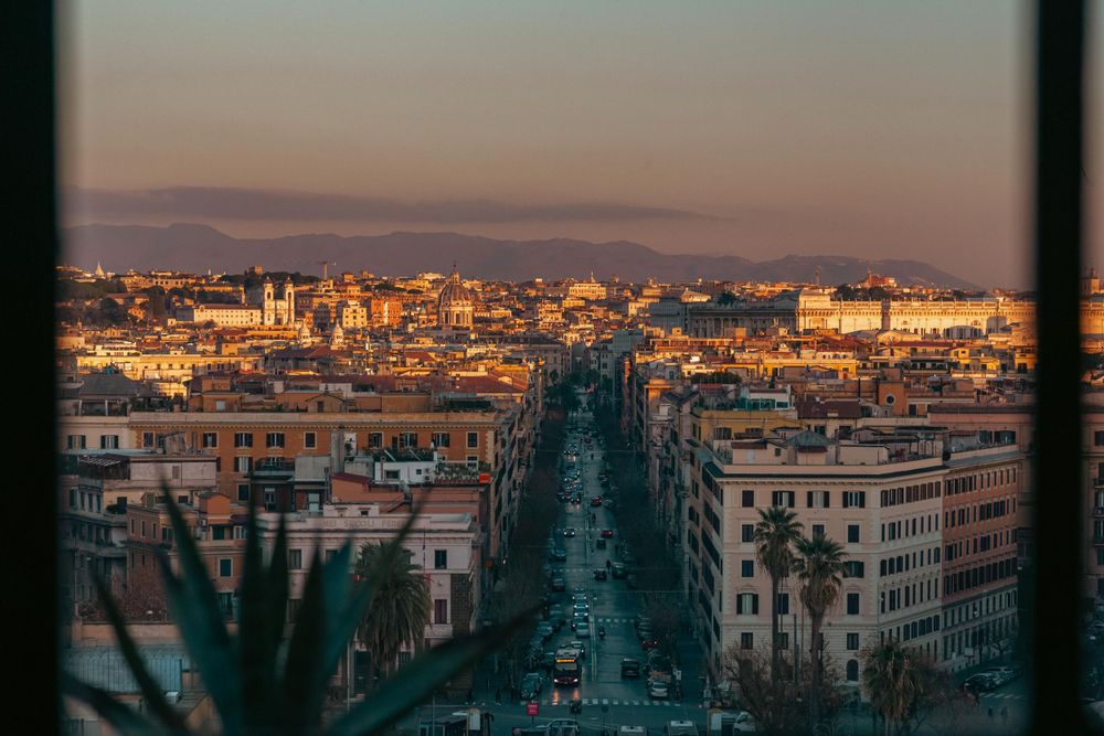 Aerial sunset view of Rome's straight boulevard lined with warm-lit buildings and palm trees.