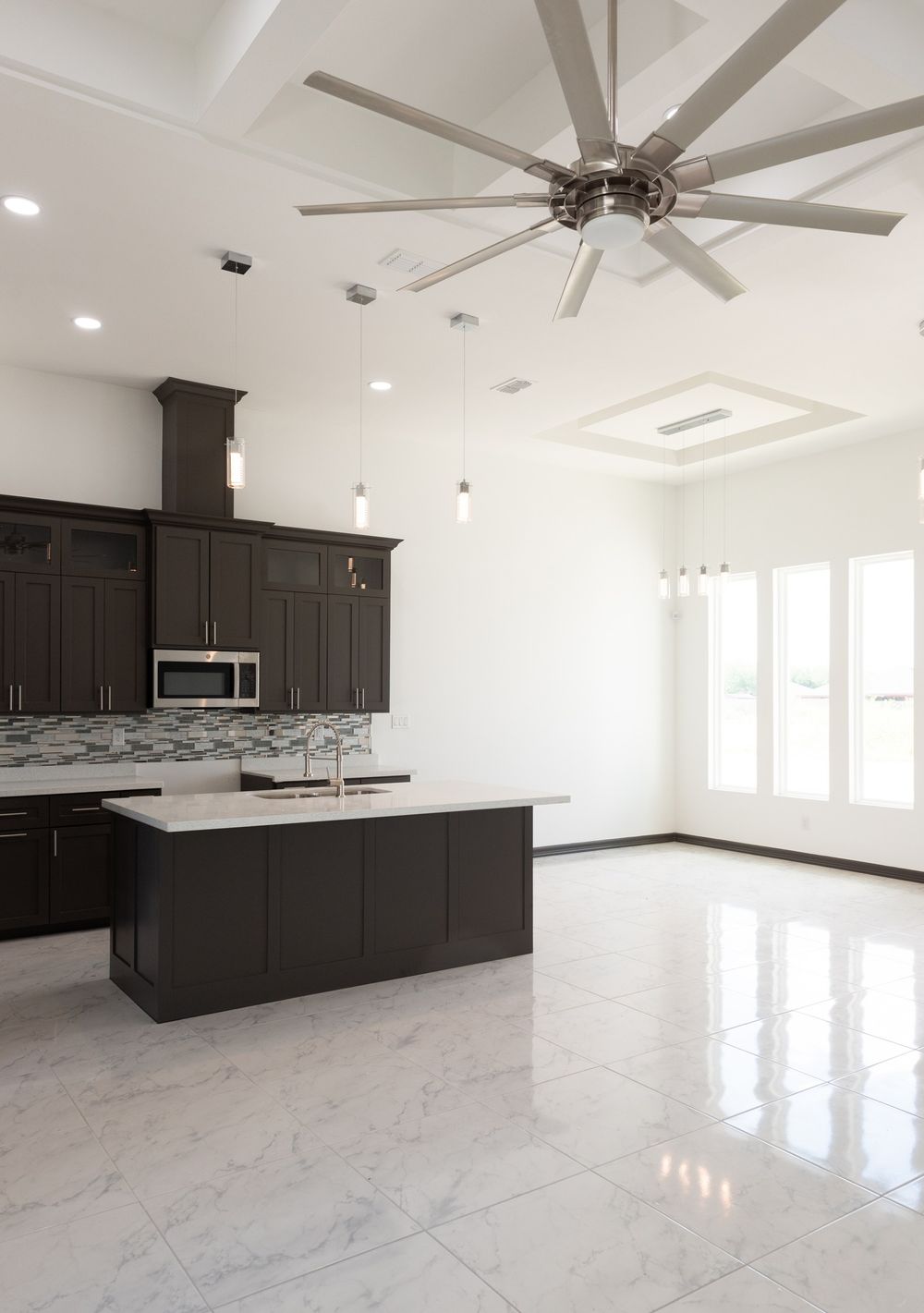 Modern kitchen with dark cabinets, marble floors and large ceiling fan in white contemporary space.