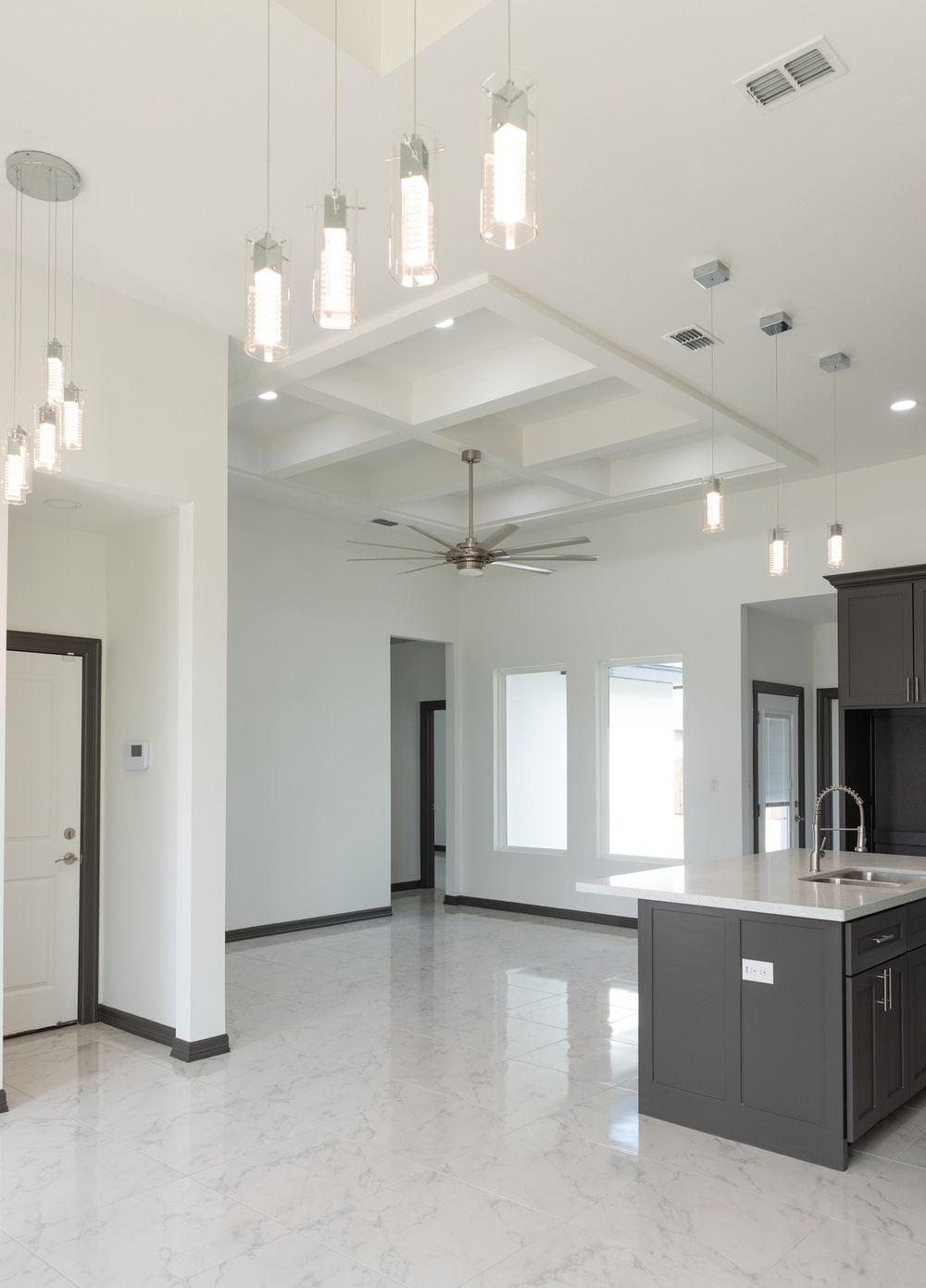 Open concept living space with high coffered ceiling, pendant lights and modern kitchen island.