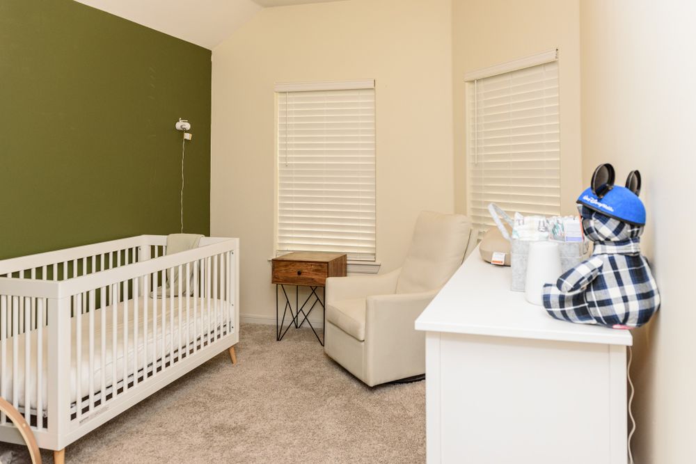 Nursery room with white crib, olive accent wall, and comfortable armchair.