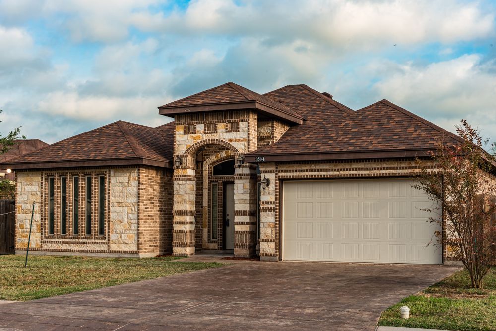 Luxury stone home exterior with brown roof, dramatic arched entrance and attached garage.