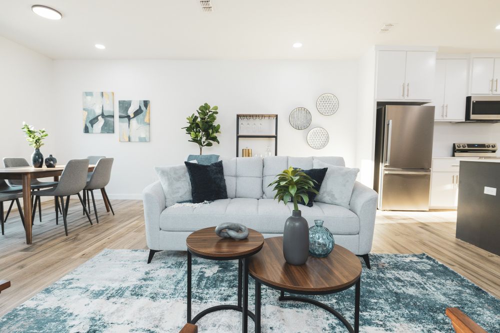 Contemporary living room with light blue sofa, round coffee tables, and dining area visible.