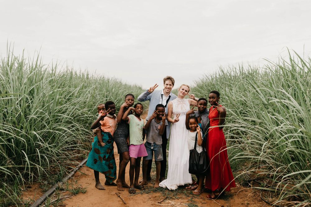 Wedding party gathered among tall sugarcane fields on a dirt path.