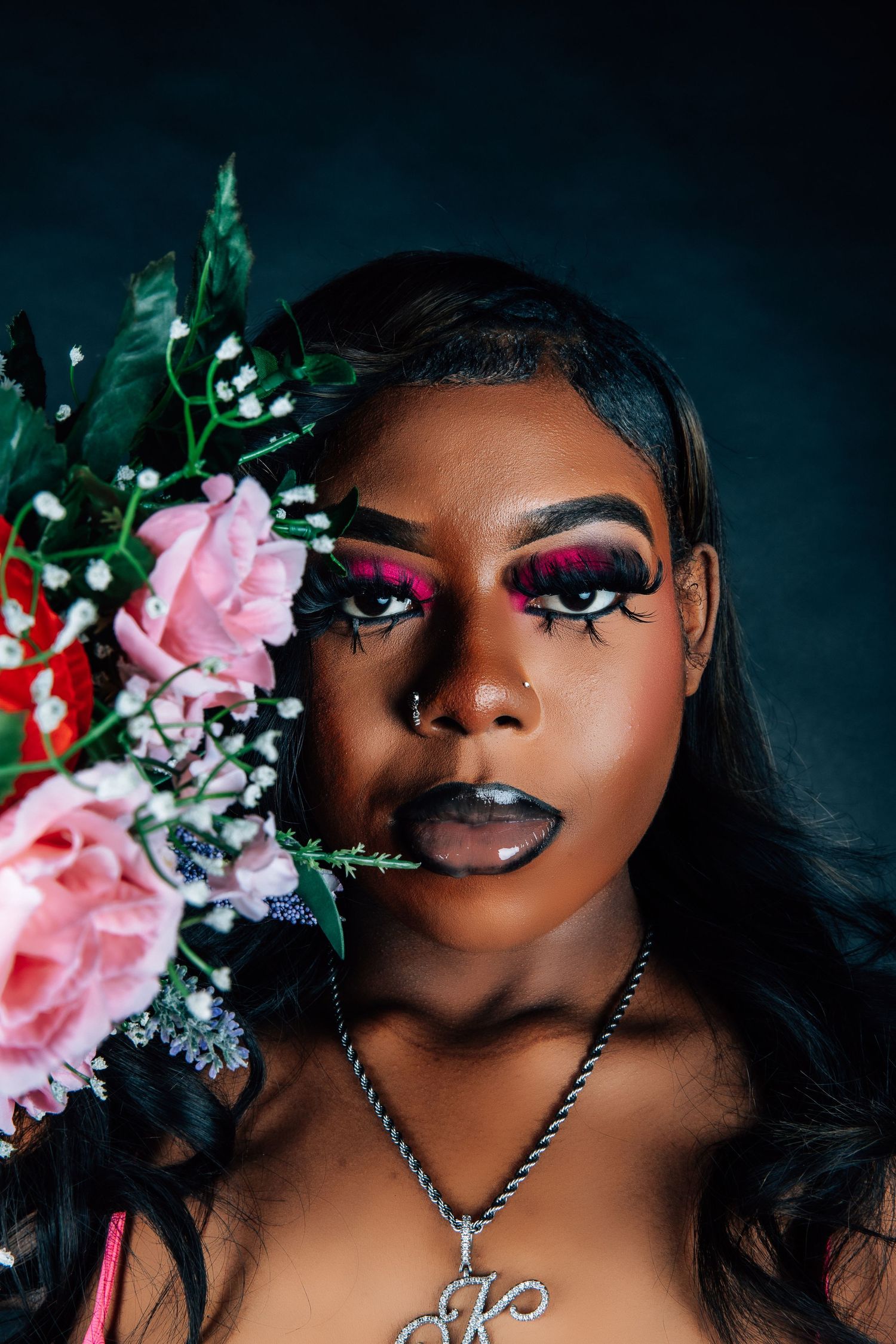 Artistic beauty portrait with pink roses and dramatic makeup against dark background.