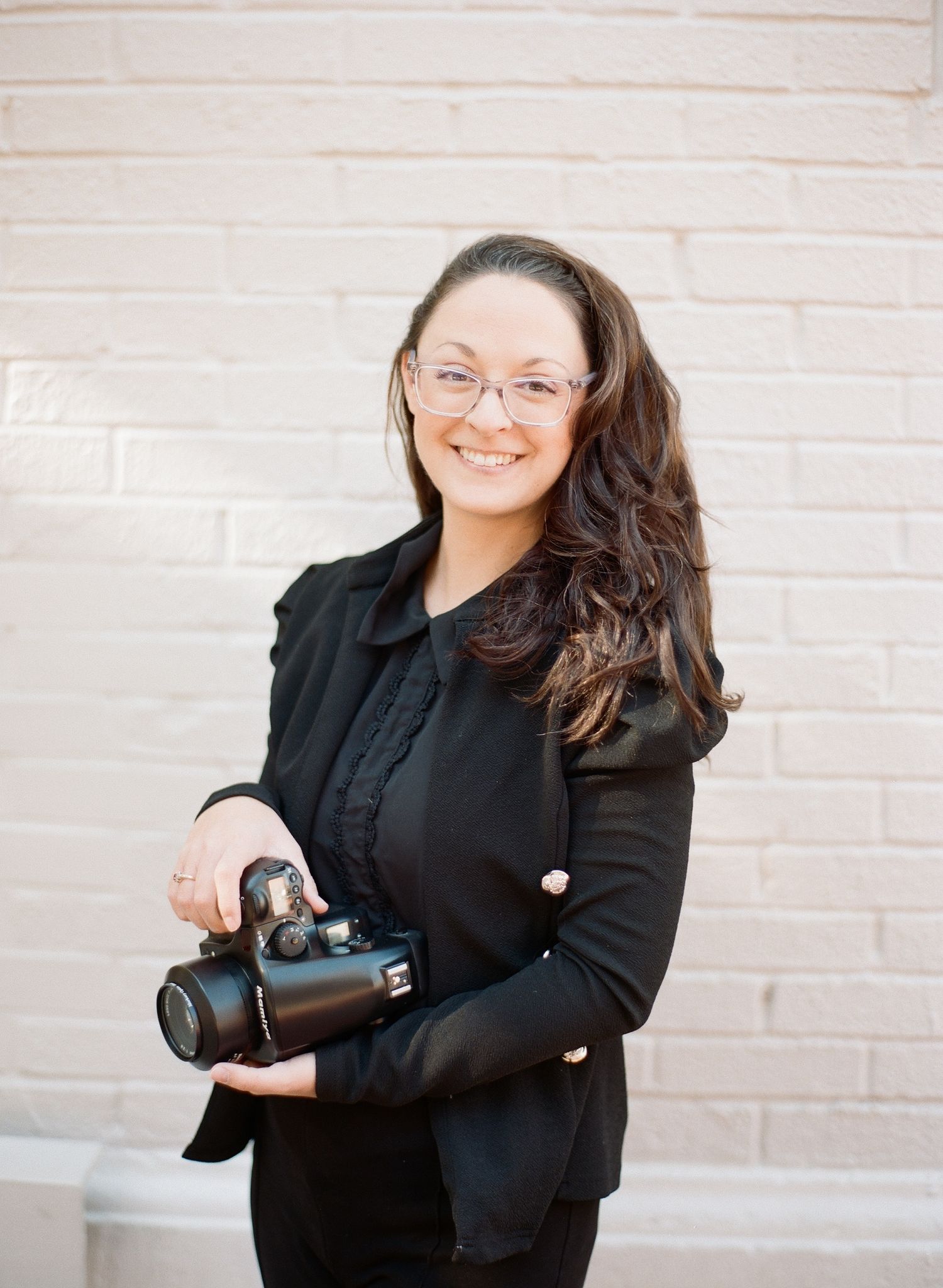 Professional photographer wearing a black blazer poses with camera equipment.