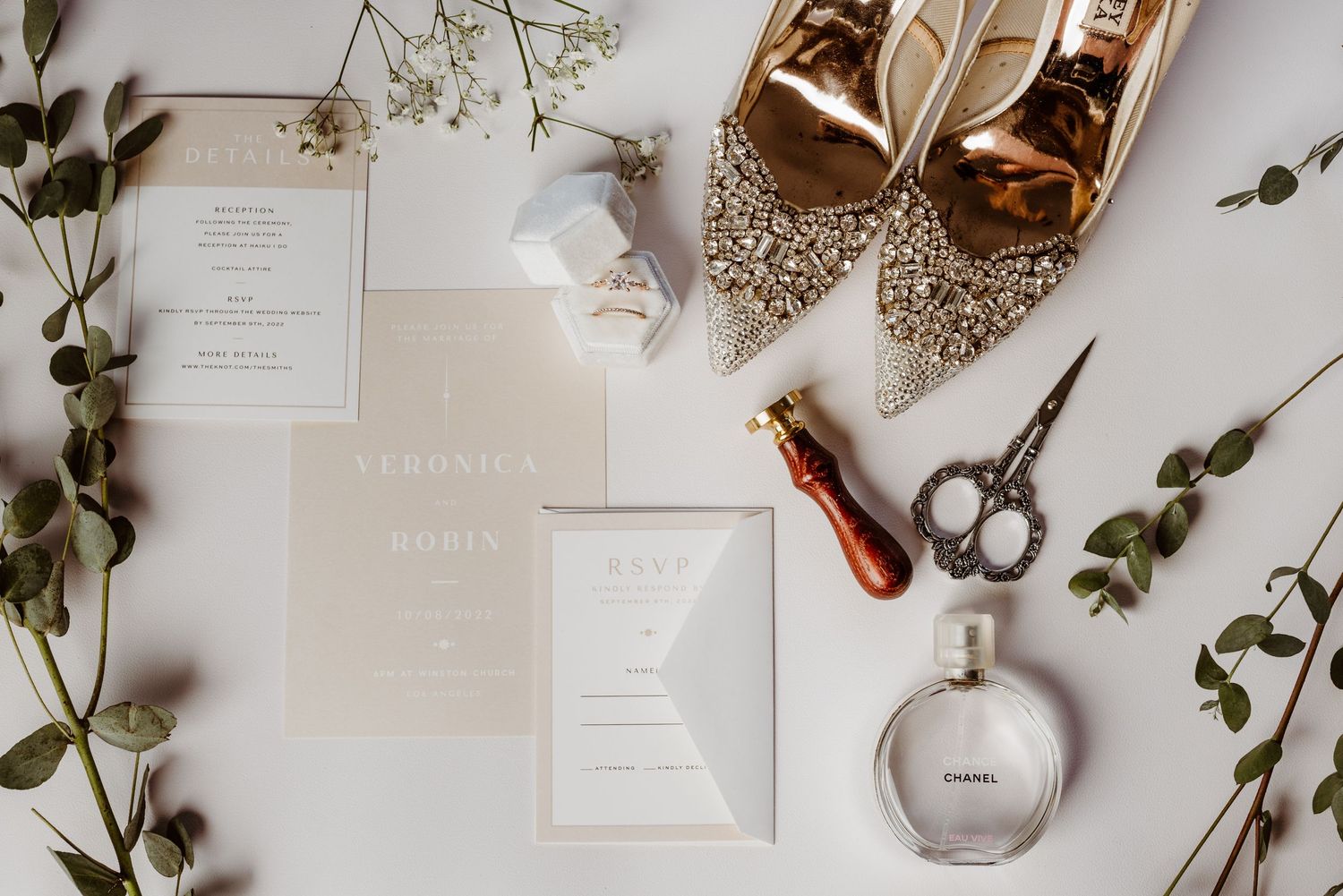 Wedding details flat lay with glitter shoes, invitations, perfume and delicate greenery.