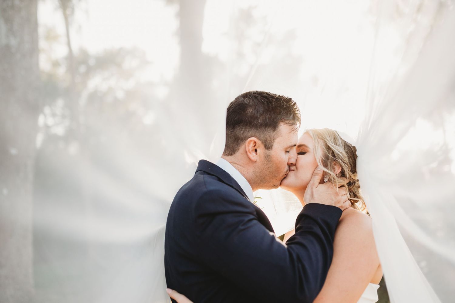 Romantic outdoor wedding portrait with soft misty background and embracing couple.
