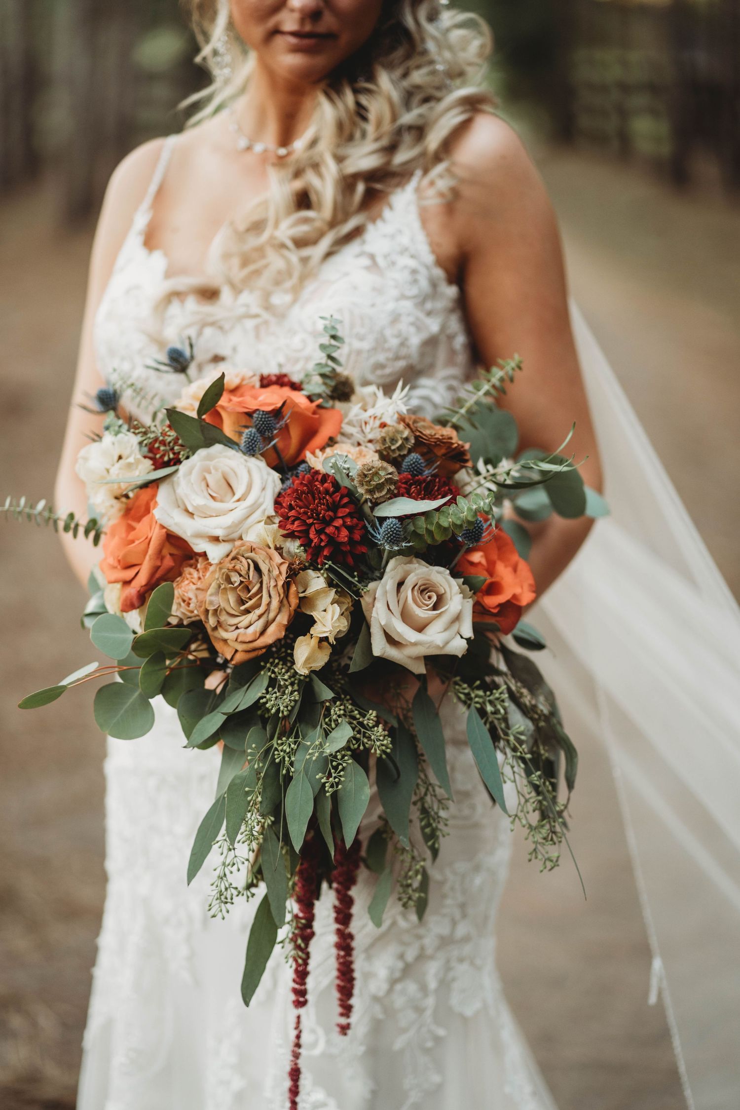 Close-up of bridal bouquet with roses, eucalyptus, and hanging amaranthus in fall colors.