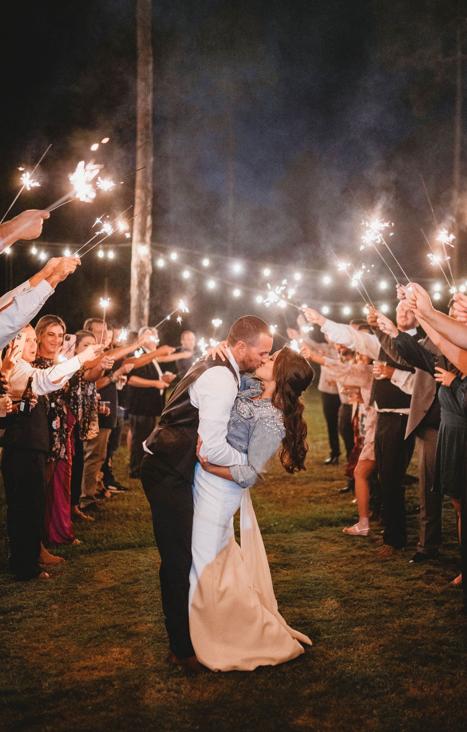 Newlyweds share romantic kiss under sparkler arch during evening wedding celebration.