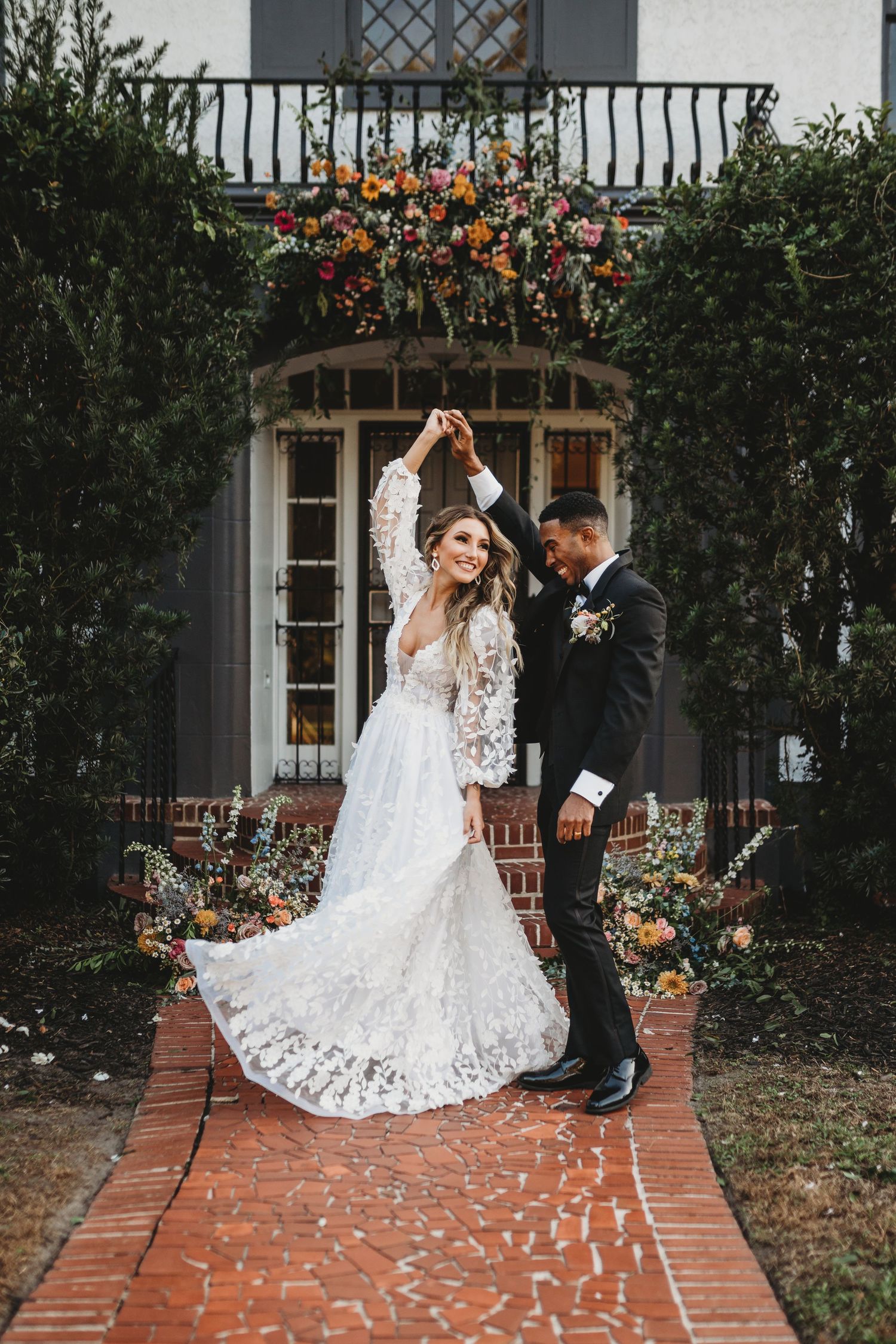 Romantic dance pose under colorful floral arch on brick pathway.