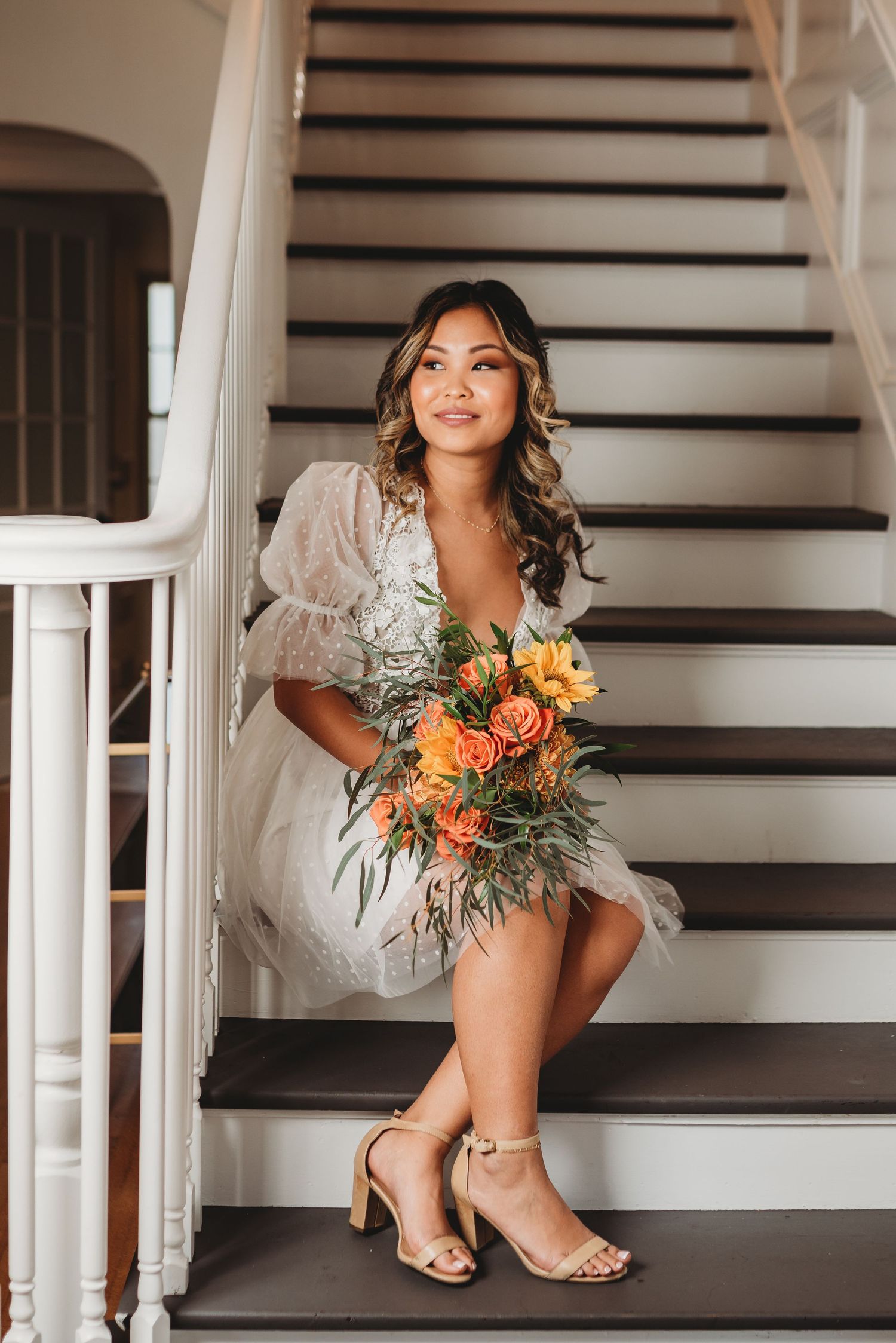 Elegant bride poses on vintage staircase holding colorful bouquet in flowing white dress.