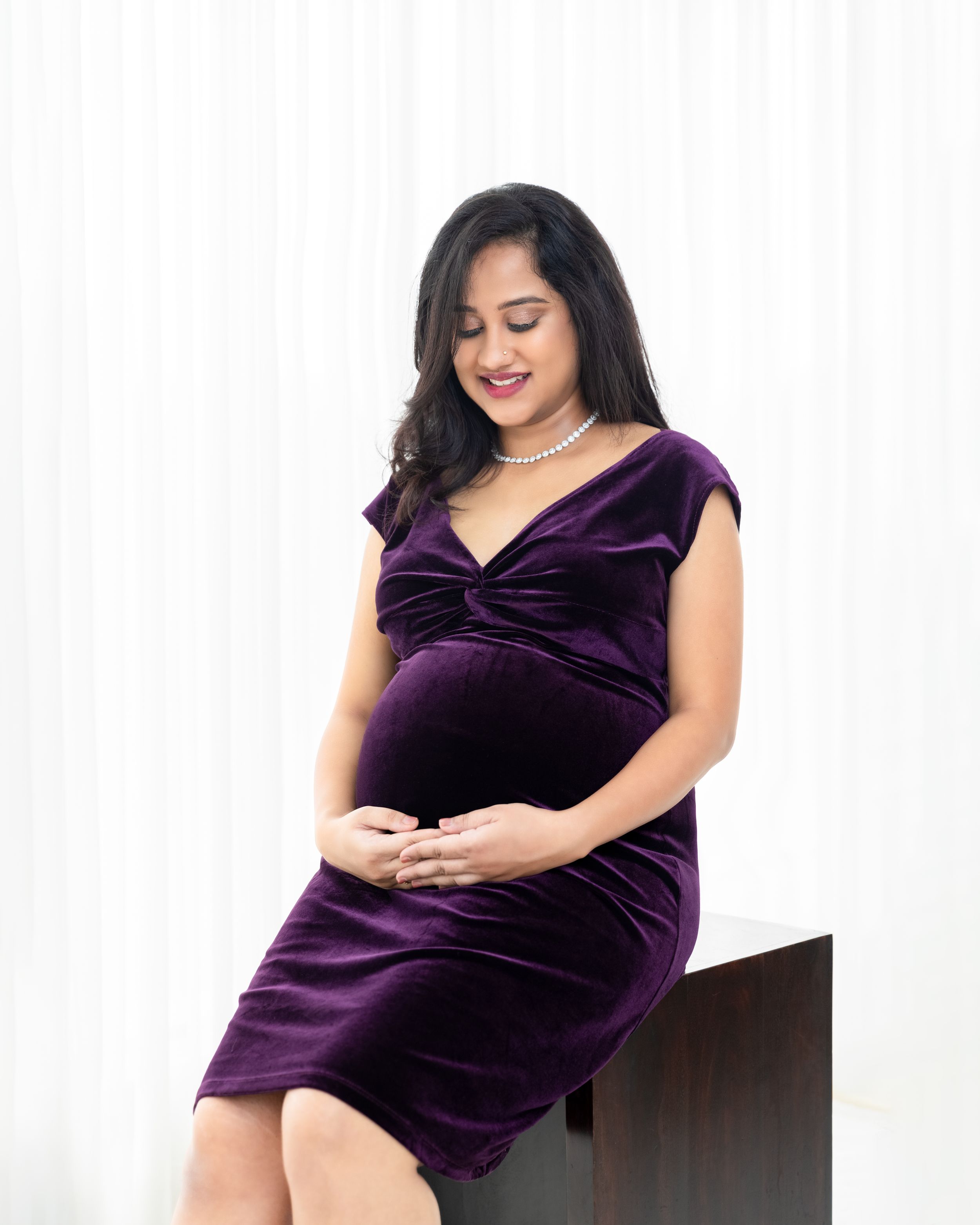 Maternity portrait showing someone wearing a deep purple velvet dress against a light background.