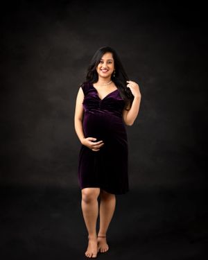 A maternity portrait featuring someone in a dark purple velvet dress against a black backdrop.