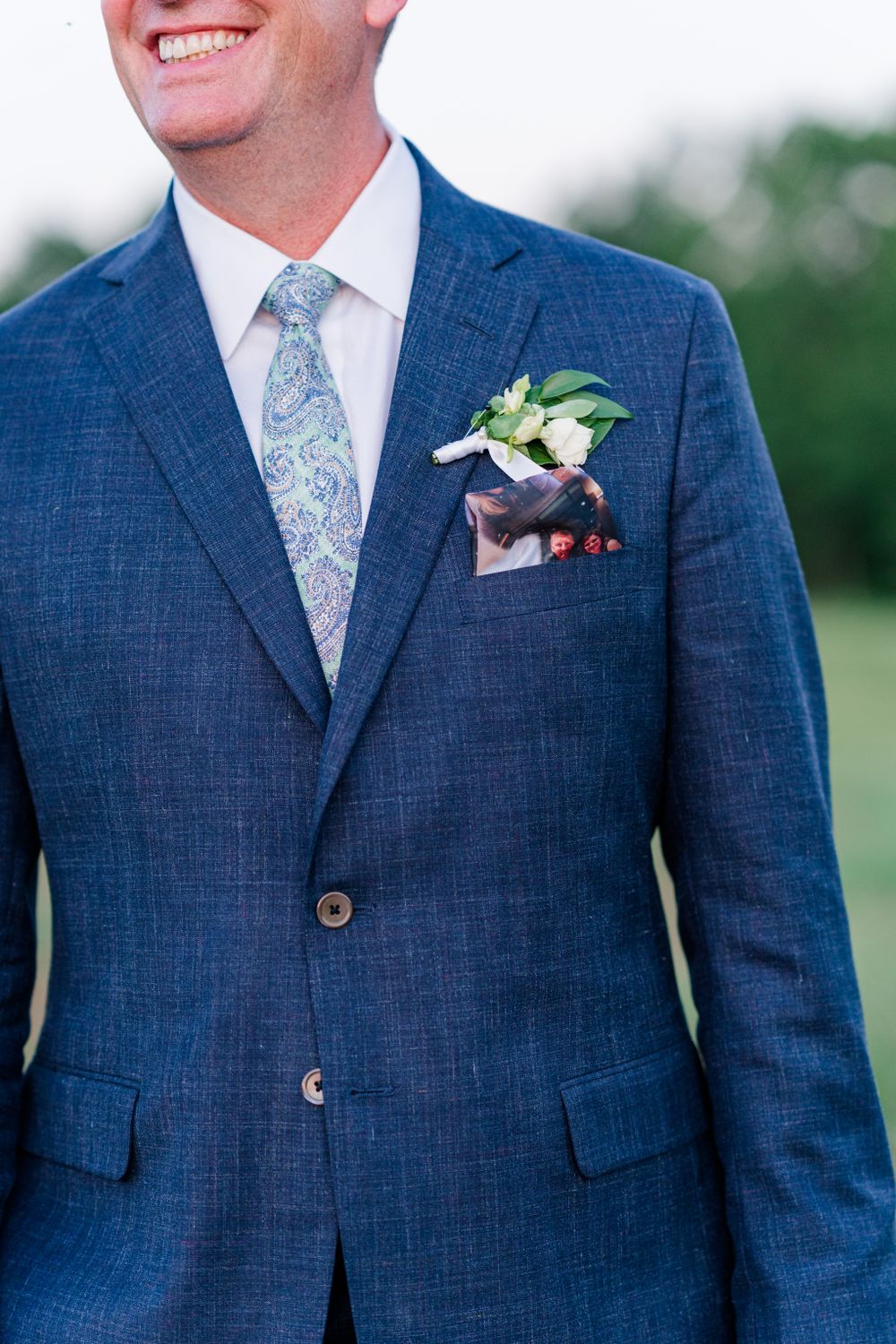 Close-up of blue textured suit jacket with floral pocket square and boutonniere.