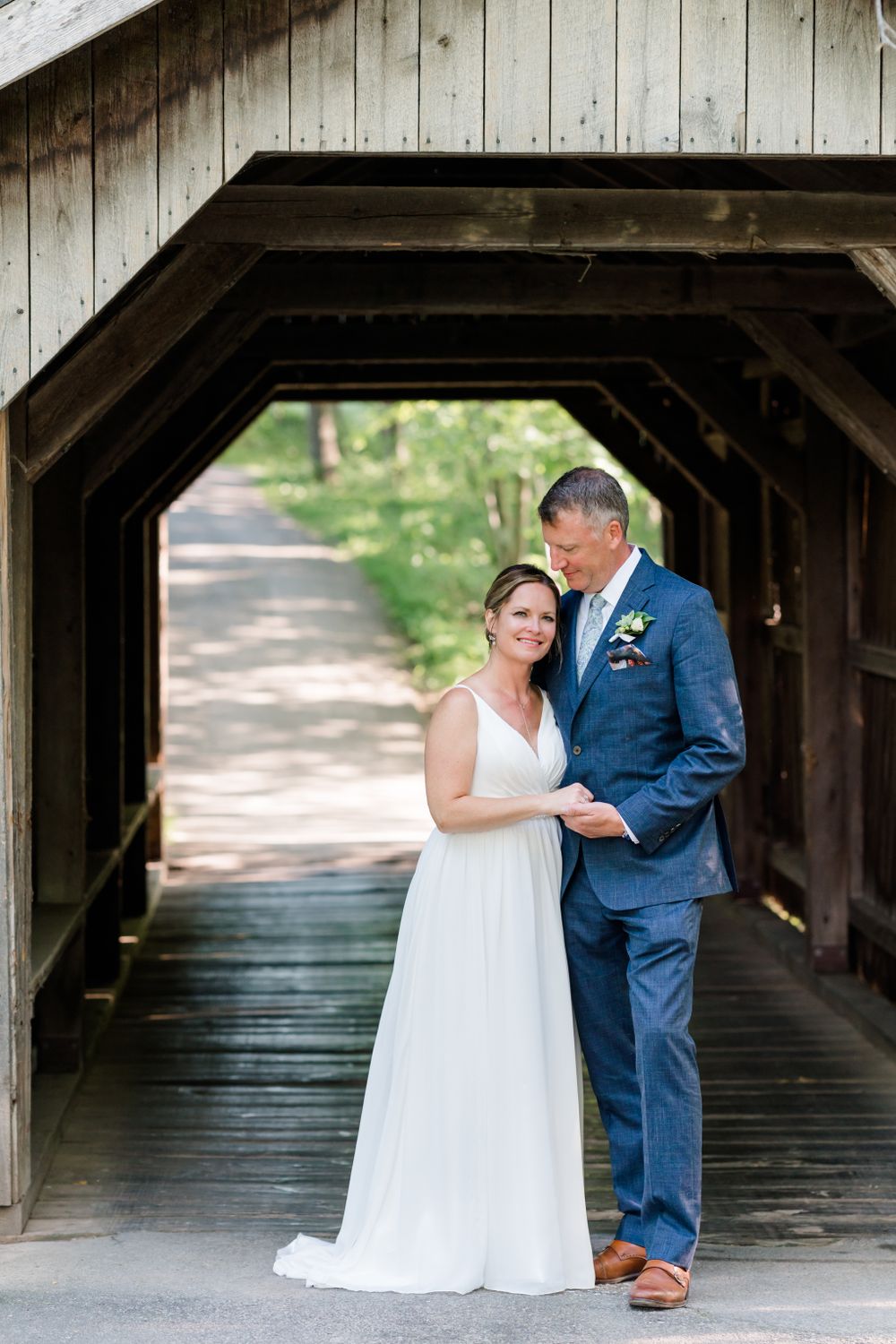 Wedding couple poses inside rustic wooden covered bridge.