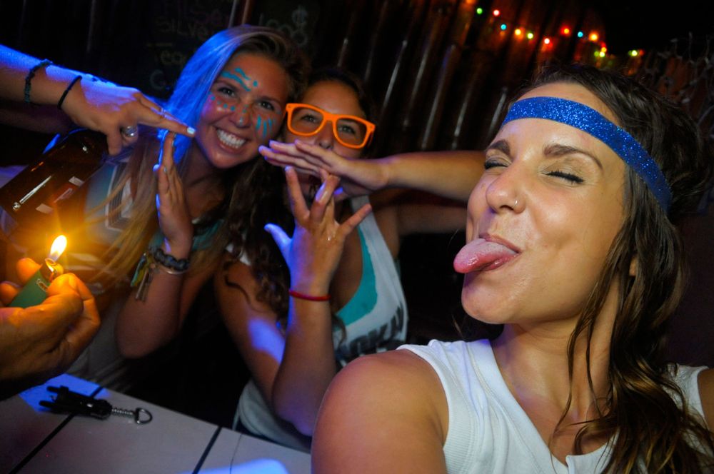 Group of people enjoying drinks at a nightclub with colorful lighting and party atmosphere.