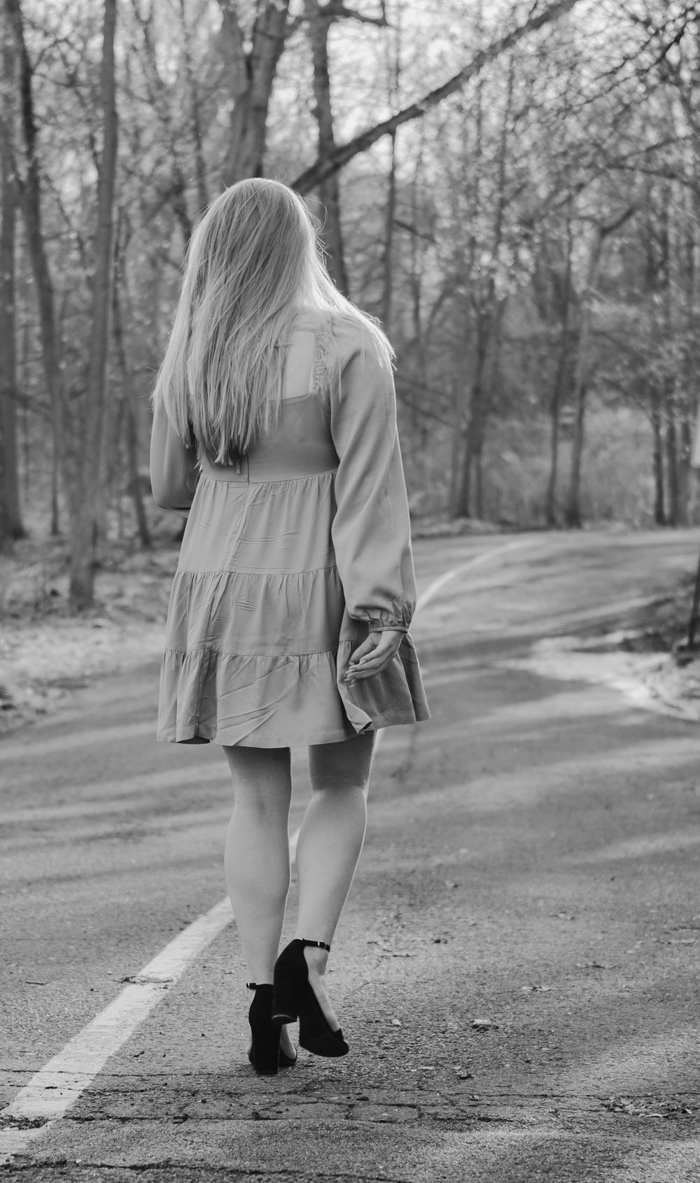 Black and white photo of a person walking down a woodland path wearing a flowing dress.