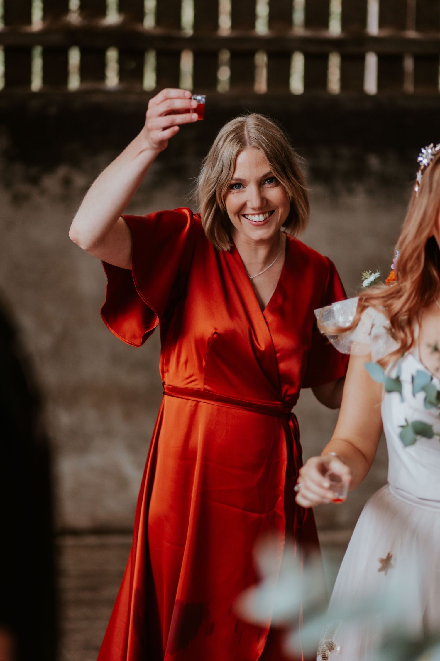 Person in a vibrant red wrap dress dancing and celebrating at an indoor event.