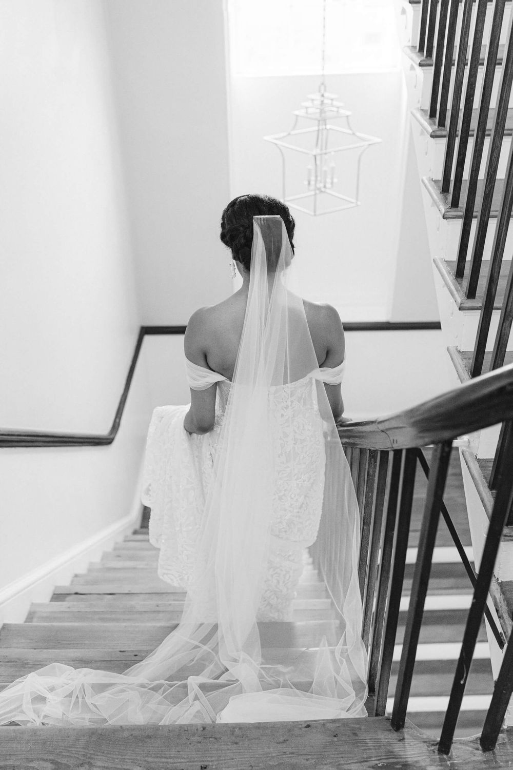 Elegant bridal portrait on stairs showcasing a flowing cathedral veil in black and white.
