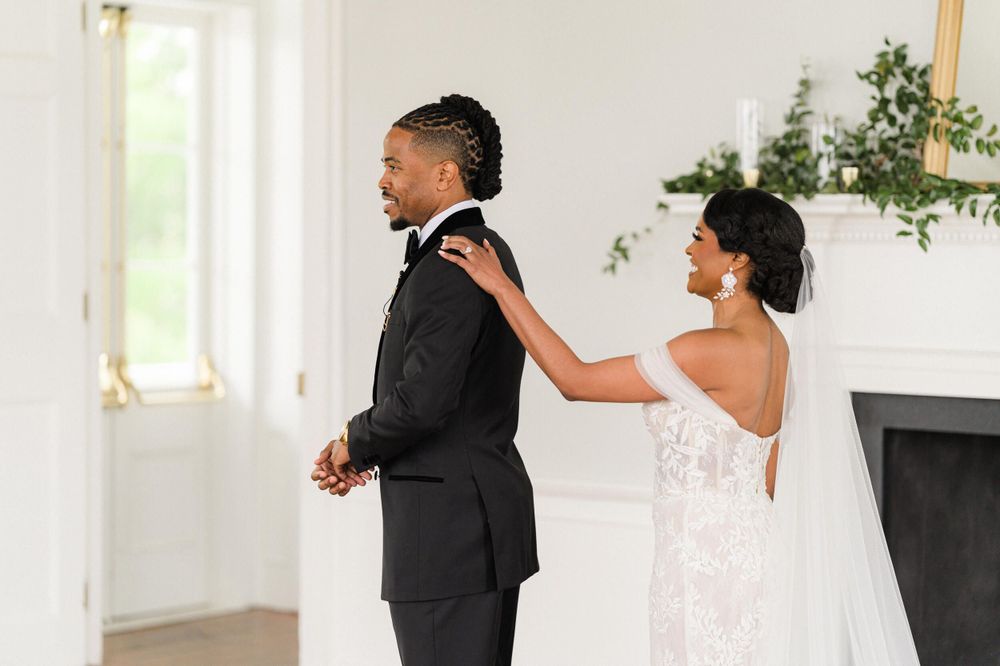 A romantic first look moment between newlyweds during their wedding with greenery decor in an elegant white room.