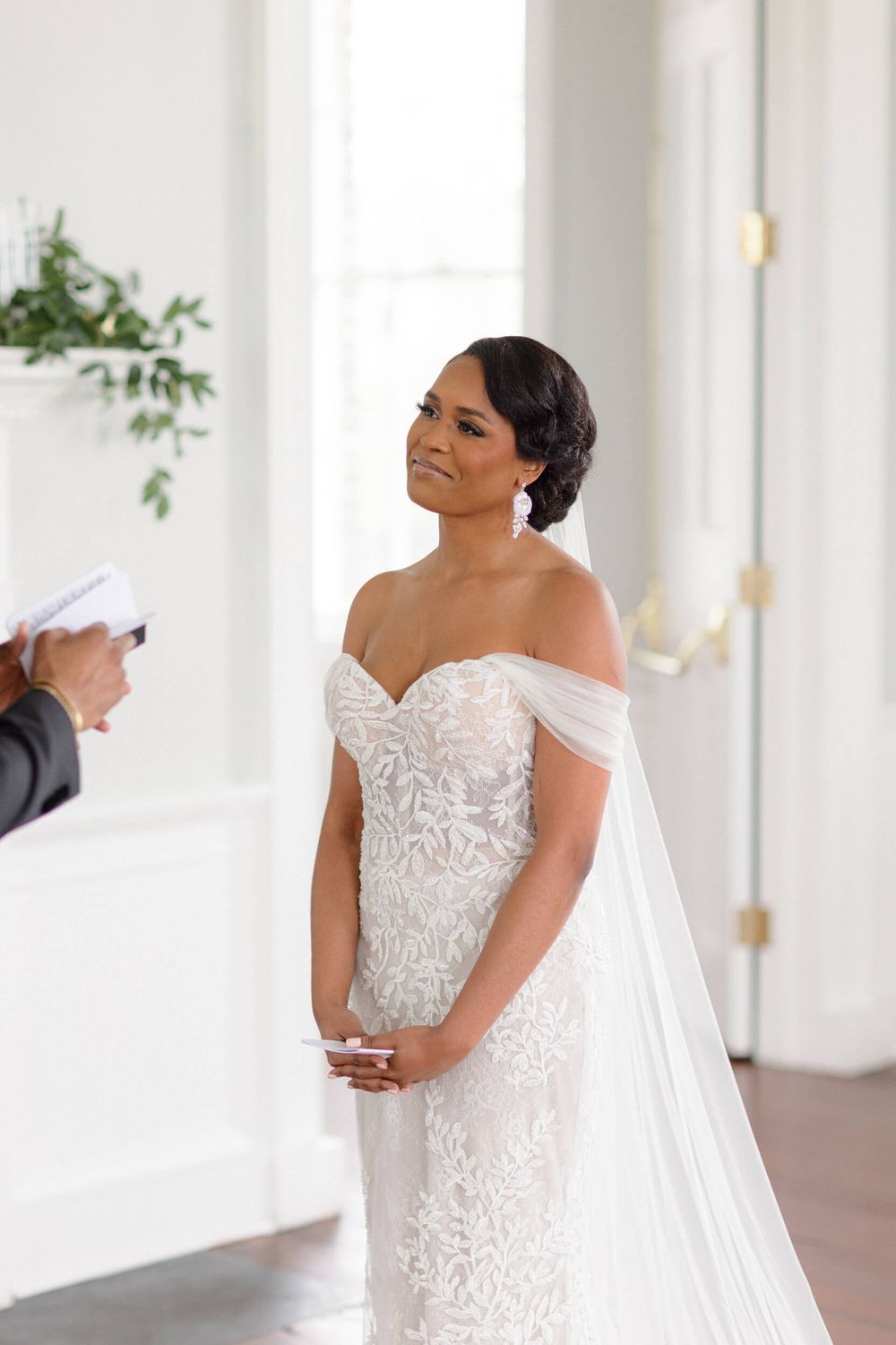 Bride in a stunning off-shoulder lace gown poses elegantly with her flowing veil.