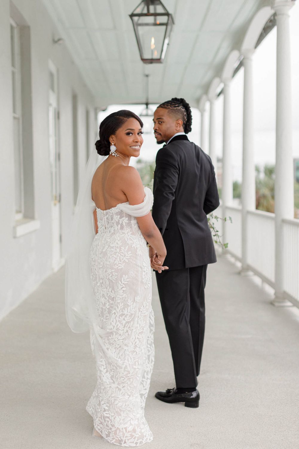 Romantic wedding couple poses in a bright white columned corridor with hanging lanterns.
