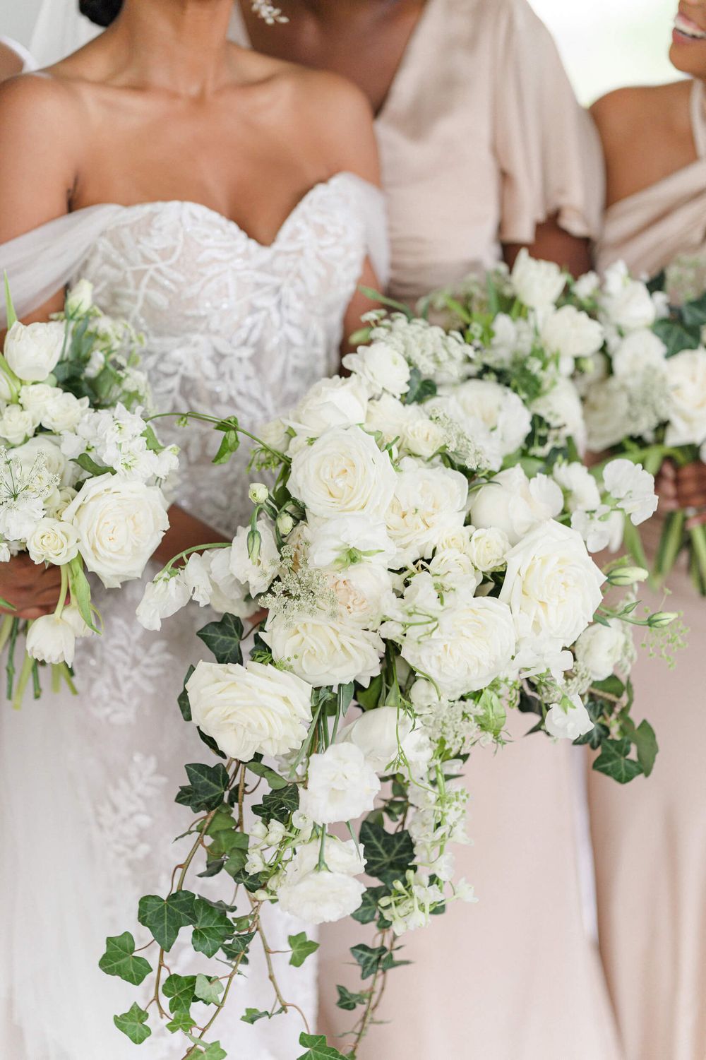 Close-up of cascading white rose and greenery wedding bouquets against blush bridesmaid dresses.