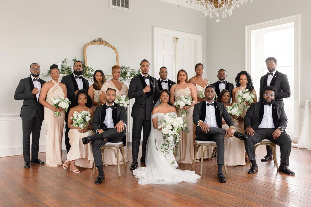 Elegant wedding party group photo in a bright white room with crystal chandelier.