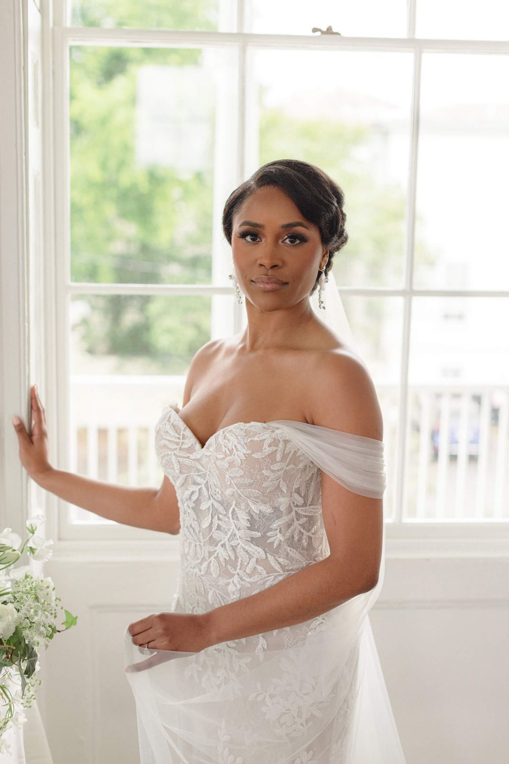 An elegant off-shoulder lace wedding gown captured in a bright white room.