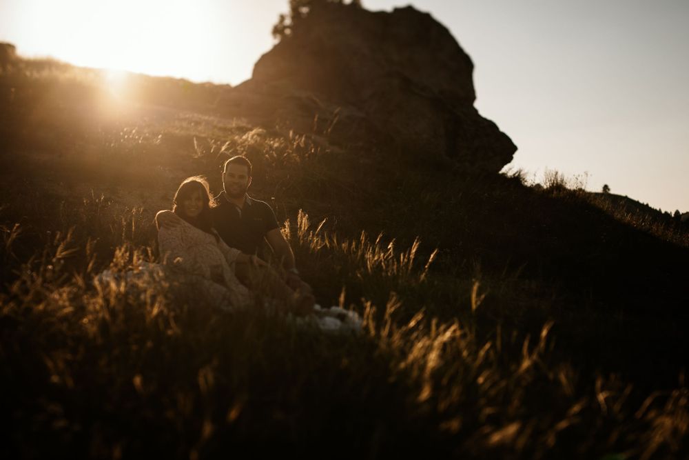 Sun sets behind rocky outcrop creating dramatic silhouette through golden grass.