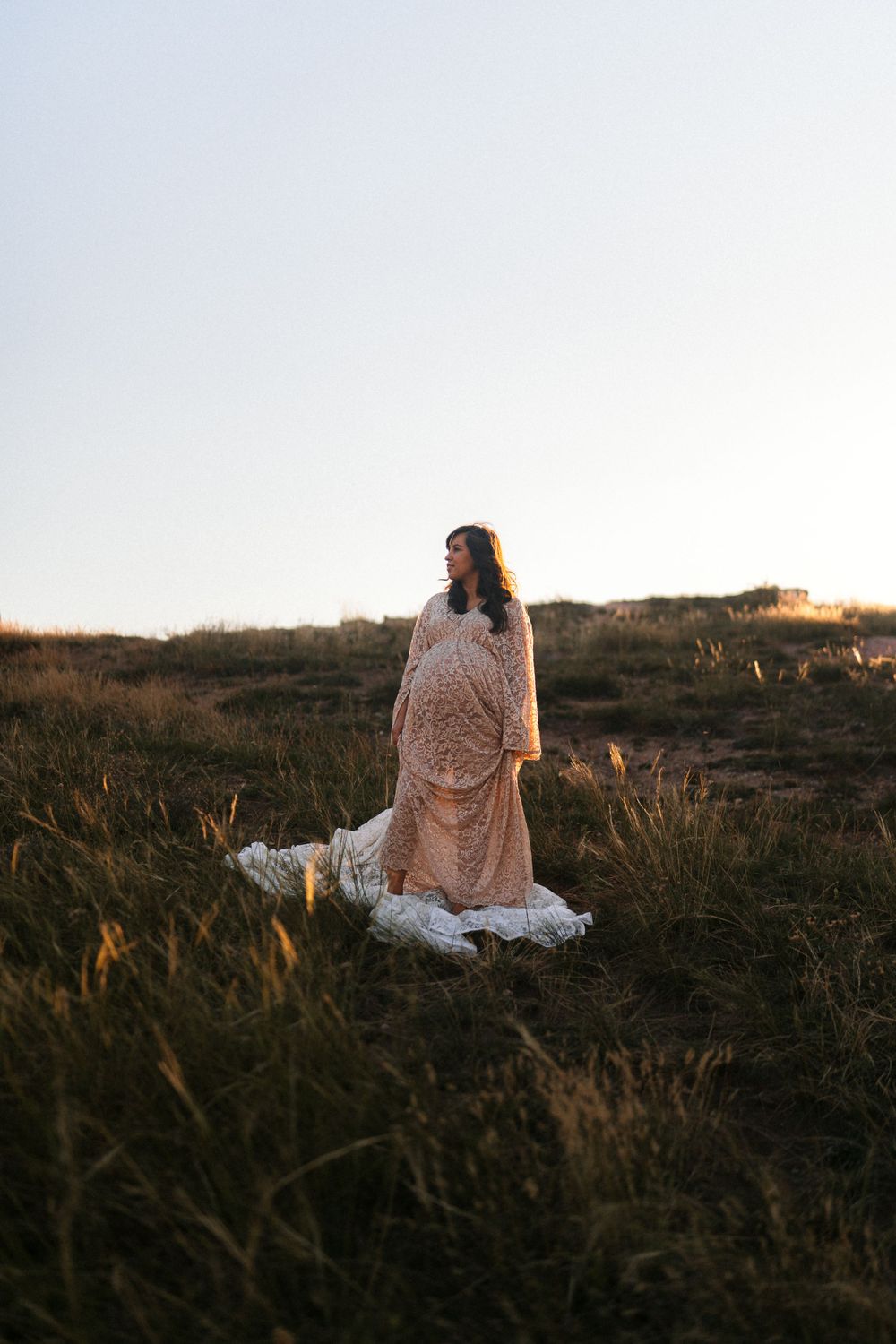 Peaceful maternity scene in lace dress amid golden grass during sunset.